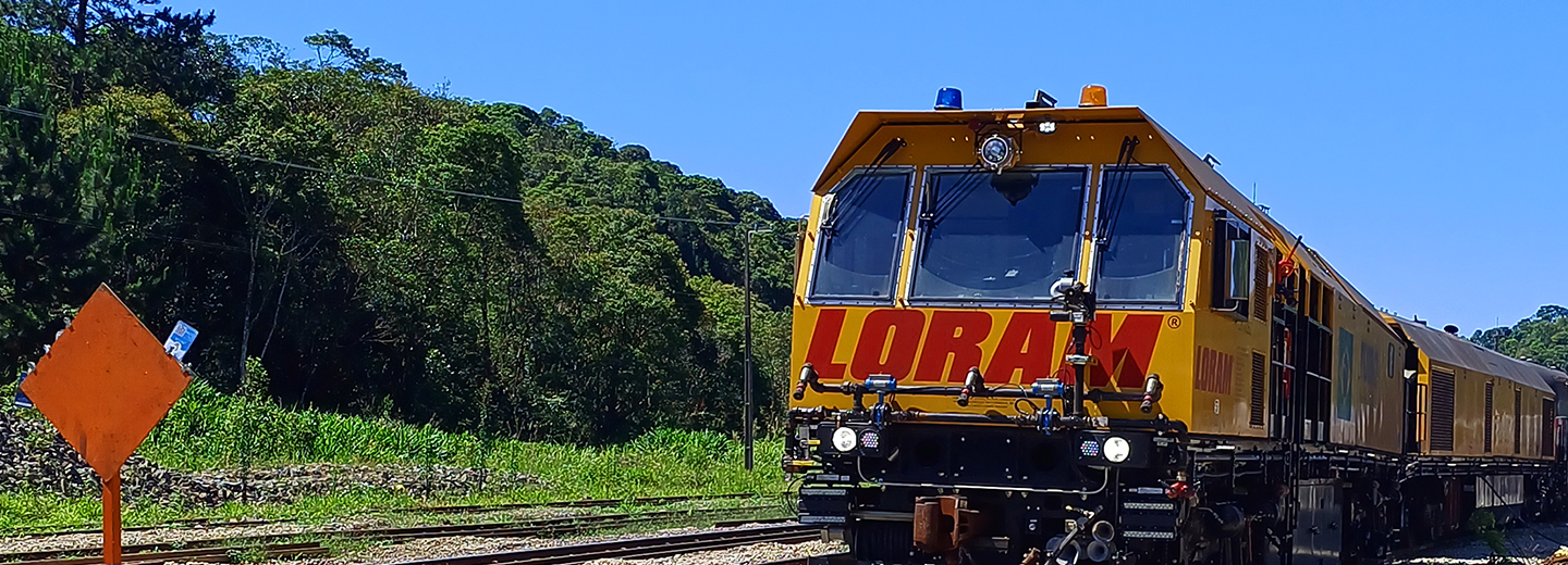 Um trem amarelo sobre trilhos, com árvores e o céu ao fundo