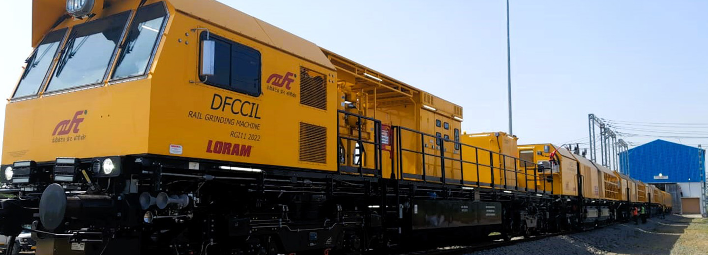 A yellow train on a track in front of a blue shed.